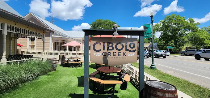 Cibolo Creek Brewing Co. Outdoor Beer Garden and Sign Exterior sign for Cibolo Creek Brewing Co. next to an artificial turf beer garden with picnic tables.